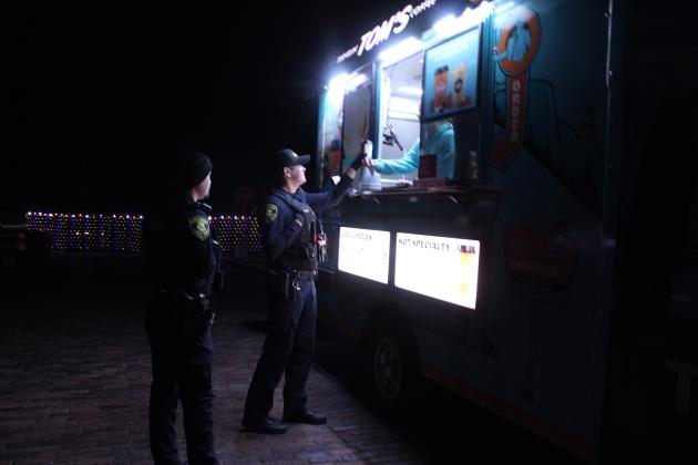Amy Sanders, co-owner of Travelin' Tom's Coffee of Shawnee, hands a coffee to Shawnee Officer Jarrett Thorpe, as Officer Isaac Clemens looks on, during the Winter Wonderland event at Santa Fe Depot on Nov. 28. There were also other food trucks and vendor booths at the event.