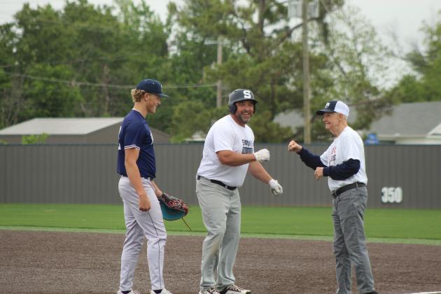 Shawnee Alumni Scott Childers gets a fist bump at first from Mike Sperry, as SHS sophomore Case Childers looks on, during the SHS Alumni Baseball Game on April 25.