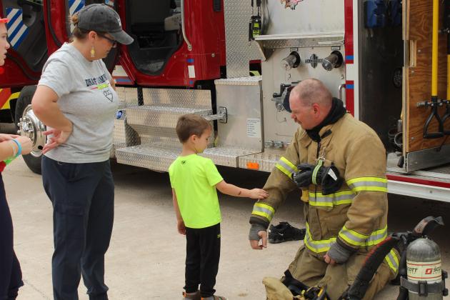 Bethel Firefighter EMR Orrin Beckham holds out his arm so Brody Hughes, 4, of Arkansas, can feel his jacket, as Amy Hughes watches, during Touch-a-Truck and Beyond, held at the CPN Festival Grounds on April 11. Organized by Pottawatomie County Emergency Management, the event also featured the Shawnee and Tecumseh Fire Departments, as well as many other agencies.