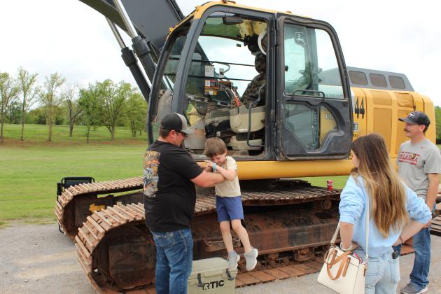 Excavator Operator Wesley Fowler lifts Kage Kile, 4, of Ada, down from the Pottawatomie County District #3 equipment, as Kile's aunt, Malorie Miller, of Stratford, watches during Touch-A-Truck and Beyond, held at the CPN Festival Grounds on April 11.