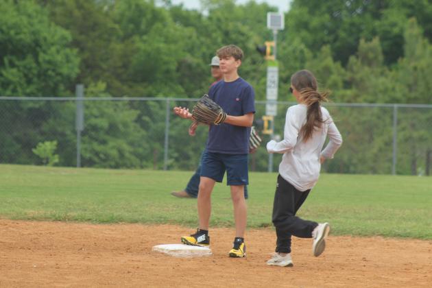 Macomb baseball player Cole Swinney waits for the ball as Macomb Special Education Director Caraline Beauchamp runs to second base during the Macomb Staff vs. Players Game on April 29. In its first year, about 12 staff members (and a couple parents) from Macomb Public Schools played members of the baseball and slow pitch teams.