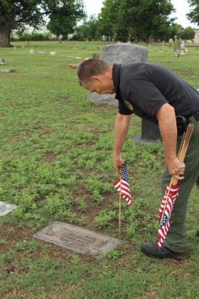 Pottawatomie County Sheriff Freeland Wood decorates the grave of Army Staff Sergeant Robert Sanders, who was in WWII, at Fairview Cemetery in Shawnee on May 23. Wood's son, Justin, and grandson, Everett Wood, 13, also helped to place flags, as they have for a few years, before Memorial Day. Photos by Natasha Dunagan, Countywide &amp; Sun