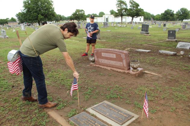 Justin Wood places a flag on the grave of Marine Sgt. Fred Bowden, as Wood's son, Everett, 13, looks on, at Fairview Cemetery in Shawnee on May 23. Wood said he, his children, and father Sheriff Freeland Wood have made this a Memorial Day tradition for several years. There were also VFW members and representatives from the Boy Scouts helping to decorate graves that morning.