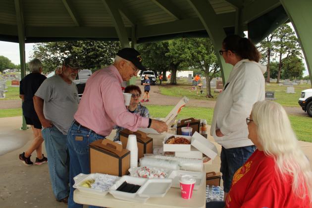 After placing flags at Fairview Cemetery, Bill Ford and James Bryce stop for donuts and coffee, provided by the Shawnee VFW Auxiliary. Those shown are Barbara White, Justine Martin and Rhonda Moore.