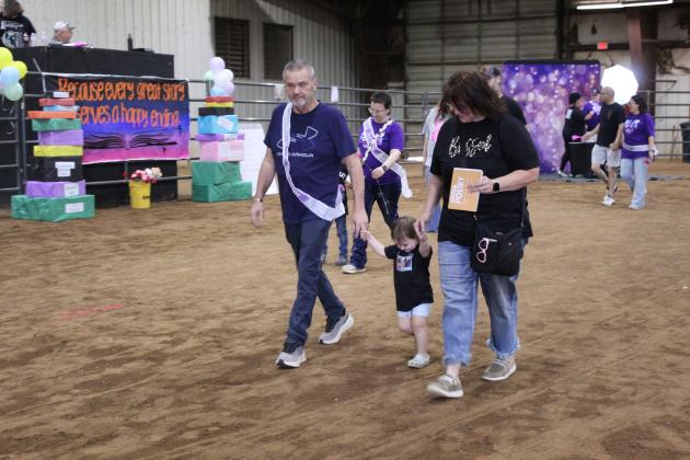 Cancer survivor William Sergio Browning and Shannon Browning of Macomb hold hands with their granddaughter, Savannah Browning, in the Caregiver Lap of Relay for Life of Pottawatomie County, held at the Heart of Oklahoma Expo Center Fred Humphries Arena on May 29. Behind the Brownings, is cancer survivor Merissa Sedlock. There were 54 registered survivors at RFL this year, and area teams raised $28,299 for the American Cancer Society.