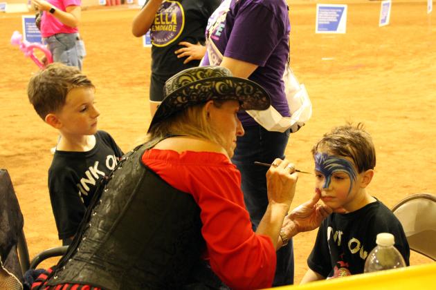 "Annie Heart" (Valarie Hames), with Creative Magic Productions in Bethel, paints the face of Jameson Sedlock, 4, as his brother, Roman Sedlock, 6, both of McLoud, watches during Relay for Life of Pottawatomie County, held at the Heart of Oklahoma Expo Center Fred Humphries Arena on May 29. The boys' mother, Merissa Sedlock, is a cancer survivor.  In addition to face painting, "Jack Spade" (Jeff Hames) juggled and twisted balloon animals that evening.