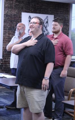 Shawnee Middle School Principal Levi Dobrinski leads the flag salute at the June 29 Board of Education meeting. Also shown are Director of Operations Matt Johnson and CFO Tristan Wyatt.