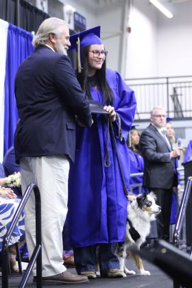 Bailee Clagg, with her miniature Australian Shepherd, receives her diploma from Bethel School Board Member Kevin Roland at the Bethel High School Graduation, held on May 16 in the BHS gym.