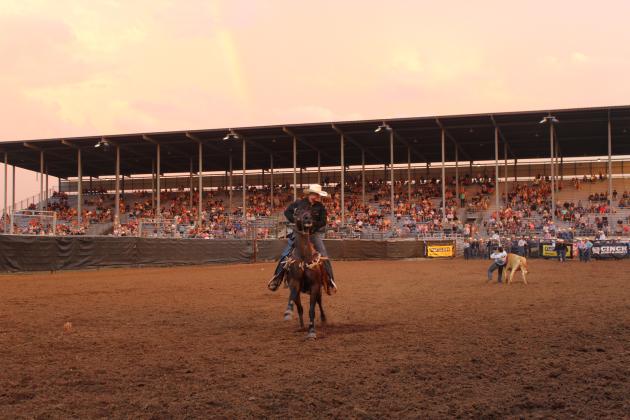 A rainbow ends at the Grandstands of the IFYR, as volunteers and contestants go about the business of steer wrestling in Arena #1 during the championship round on the evening of July 17.