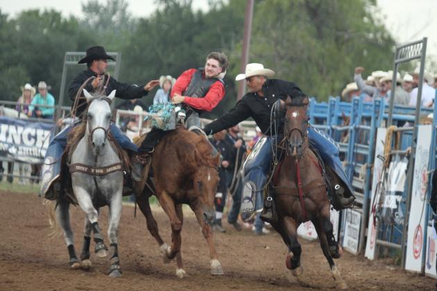 Bryer Prince of Sulphur, LA, gets help dismounting from rough stock pick-up men, Sean Prater and Brandon Harris, during the bareback bronc event of the IFYR championship round on the evening of July 17. Prince placed fourth in the overall event standings.