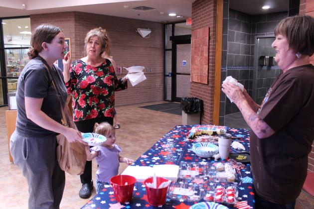 Mary Simms serves cake to Alyssa Wissinger and Brielle Jackson, 2, both of Shawnee, as Deedee Thomas of Tecumseh looks on, during the third day of 250th USA anniversary celebrations in the library lobby on July 1. They offered popcorn and ice cream sandwiches on June 29, and the Snow Shak offered free snow cones at the library on June 30.
