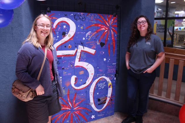 Oklahoma Baptist University graduates Linnea Malmberg, left, and Abigail Ryan pose by a community tile artwork, which they coordinated since May, during the "Pop In to Celebrate America's 250th Birthday with Popcorn and Ice Cream" event at Shawnee Public Library on June 29.  - Photos by Natasha Dunagan, Countywide &amp; Sun