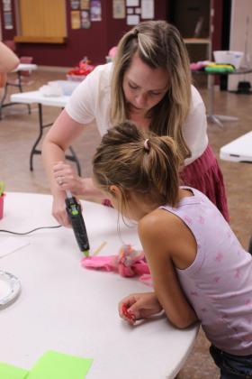 Shawnee Public Library Children's Librarian Haley Michael helps Melody Geissler, 8, of Shawnee, with the hot glue gun while working on her sock puppet during the "Creativity Unleashed: Crafternoon for Kids" program on July 22.