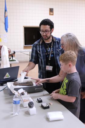 Science Museum Oklahoma Educator Calen Cavallaro shows a 3D-printed T-Rex tooth and his collection of purchased fossils, as well as a fossilized T-Rex thumb, to Linda Jones and her grandson Kyler Wiley, 8, both of Tecumseh, at the "Dino or Not? The Ultimate Prehistoric Showdown" program at Tecumseh Public Library on July 16. Cavallaro also brought several 3D-printed dinosaur skulls and spoke about what qualifies as a dinosaur.