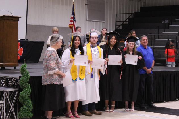 Mary Hopper, with the Maud Alumni, and John Tredway, with the Maud Masonic Lodge, present four scholarships to Abigail Horton, Crew Peters, Natalie Brown-Harjo and Addison Bird during the Maud High School Graduation on May 22 at the Ed Harman Gymnasium. They granted seven $1,000 scholarships, but not everyone was present.
