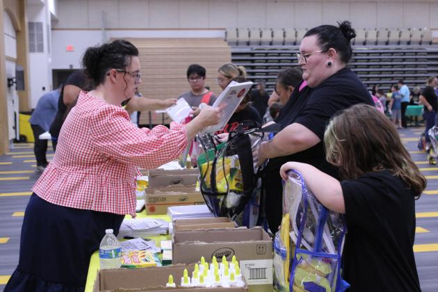 Volunteer Christal Jones adds notebook paper to the backpacks of a mother and daughter during Mission Tecumseh's annual Back to School Bash, held at the Tecumseh High School W.P. Wood Alumni Center on July 25. Mission Tecumseh, which includes six local churches, offered 500 clear backpacks, five school supply stations, a prayer station, craft area and free hotdogs and watermelon. Rev. Anthony LaGrange said they estimate that 750 to 800 people attended the event, Saturday.