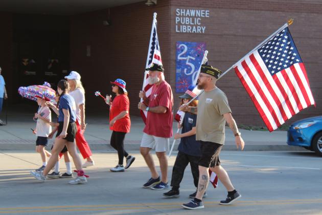 Shawnee VFW members, Past Commander Patrick Koch, Killian Keathley and Michael Keathley, carry flags in the Shawnee Independence Day Parade on July 4. Shown in the background is the Shawnee Public Library's community tile artwork celebrating the 250th USA anniversary. The parade started at the Pottawatomie County Museum at 7:30 am and ended at Woodland Veterans Park with a presentation.
