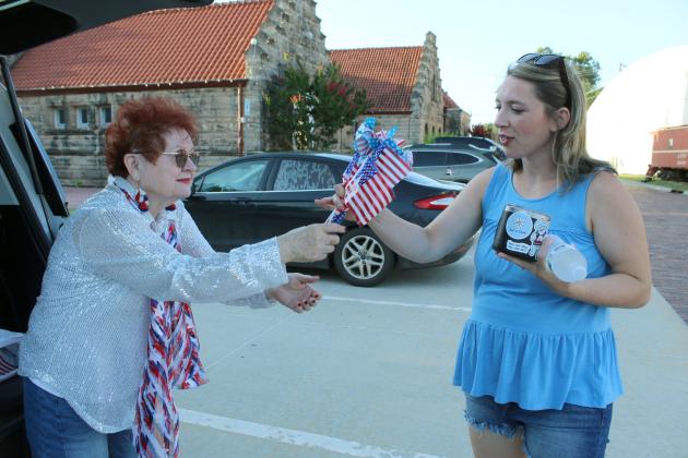 VFW Auxiliary President Barbara White hands flags and flag pinwheels to Maddie Urton of Shawnee for her family before the Shawnee Independence Day Parade on July 4, which started at the Pottawatomie County Museum.