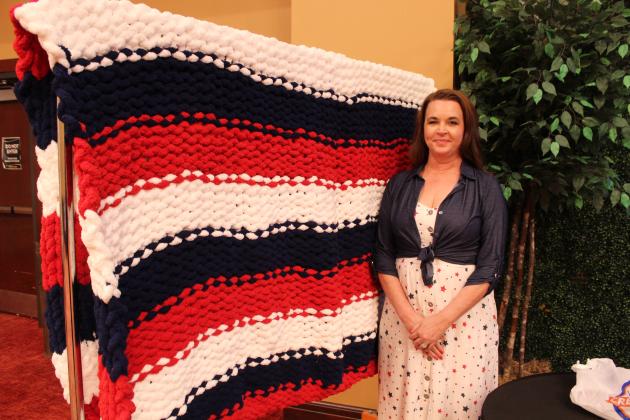 Lisa Snodgrass poses with a queen-sized afghan, which she hand-knitted with chunky yarn, during the American Legion Auxiilary Department Summer Convention, held at the Grand Casino Hotel and Resort on July 12. A drawing for the afghan will be held at the Tecumseh American Legion Post 260 on Veterans Day, and tickets are now for sale. Snodgrass is the daughter-in-law of Donna Snodgrass, who was sworn in as the American Legion Auxiliary Department of Oklahoma President that day.