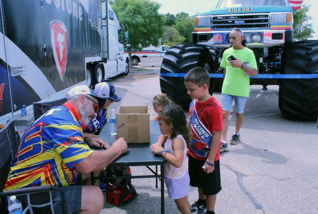 Bigfoot driver Garrett Hicks signs autographs for Kimaja Daniels, 3; Amajee Daniels, 6; and Ka'mora Daniels, 2, all of Seminole, as David Brewer asks about the monster truck and Theresa Hicks sits beside her husband during the Eighth Annual Cops N' Kids, held on Aug. 22 at the Heart of Oklahoma Expo Center. G. Hicks said the retired Bigfoot truck on display is number eight, and they are up to number 25 in the international Hot Wheels Monster Truck Live circuit. Photos by Natasha Dunagan, Countywide &amp; Sun