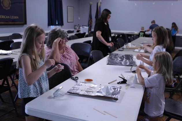 Kelly Lempges, second from left, watches her granddaughters construct protective breast plates that would hold up to a hit from a Stegosaurus tail during the "Impact Engineering: Outstanding Dinosaurs" McLoud Public Library program, held at the American Legion Ray Large Post 244 on July 30. Those doing the building are Molly Lempges, 7, far left; Stella Lempges, 8; and Mattie Lempges, 4. Also shown, in background, is McLoud librarian Trisha Bias.