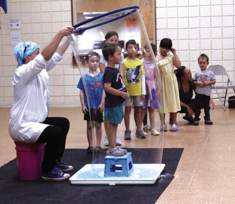 Professor Bucket makes a bubble around Shepherd Oldham, 3, of Tecumseh, as a line of children waiting to do the same watches during the 'Bubble Party' at Tecumseh Public Library on July 31. Natasha Dunagan, Countywide &amp;amp; Sun