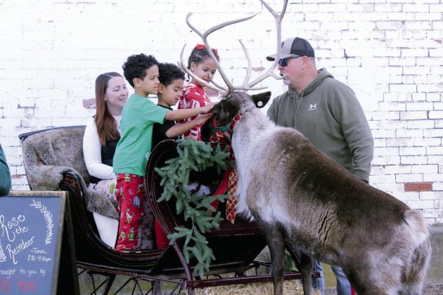 Titus Hancock, 6; Malachi Hancock, 5; and Emersyn Hancock, 7, all of Meeker, pet Rose the Reindeer, as Jamie Hancock and reindeer wrangler, Nick Ledbetter, watch and supervise at The McLoud Mercantile on Dec. 20. Rose comes from the Reindeer Club in Bristow, and Mercantile co-owner Samantha Sessums said in a video on their Facebook page that she has been trying for three years to get the live reindeer there. This year, there was a cancellation and a last-minute opportunity.  See full cutline below.