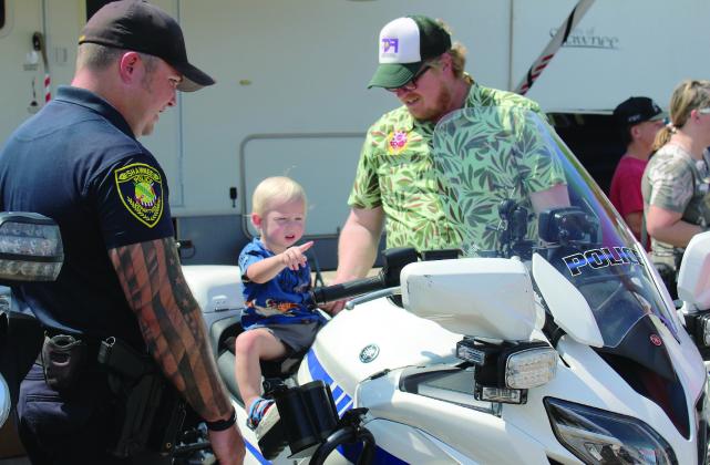 Finley Fry, 17 months, of Shawnee, sits on a Shawnee Police Department motorcycle and points at something, as Corporal Josh Soward, far left, and Fry's father, Matt Fry, keep watch at Cops n' Kids, held on Aug. 24, 2024, at the Heart of Oklahoma Expo Center. File photo