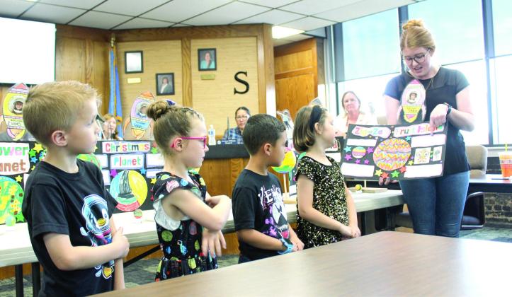 Led by Shawnee Early Childhood Center Teacher Hannah Jett, Sadie Dobrinski reads what she wrote about her planet, 'Zig-Zag Fruit Island,' during the May 5 Shawnee Board of Education meeting. Also shown, from left, are Kaidyn Sowder, Isabel Delgado and Mason Anderson, who spoke about their planets as well. Natasha Dunagan, Countywide &amp; Sun
