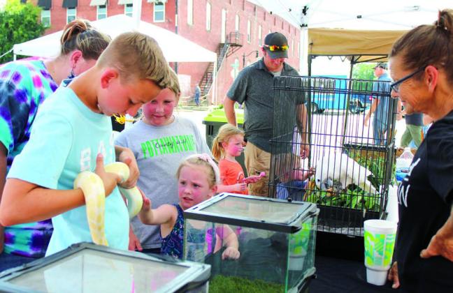 Preston Haines, 14, of Tecumseh, holds an albino ball python as Abigail Townsend, 4, of Macomb, pets the snake and Hailey Townsend looks on at the Tiger Safari booth during the Mingle on Main Street Block Party in Tecumseh, June 20.