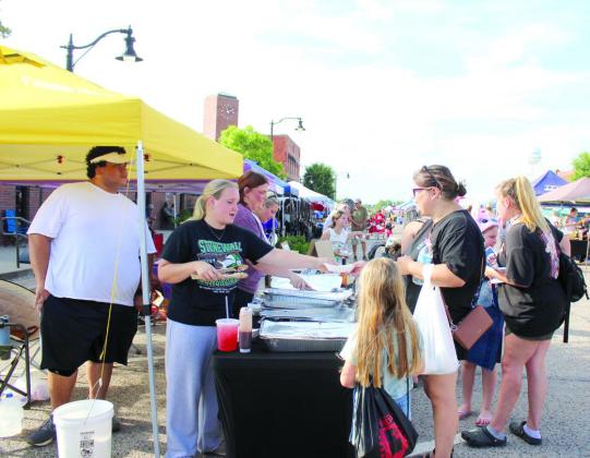 Home Church members Tara Ashcraft, Tatum Kuhn, and Jami Smith offer samples of grilled or smoked meat from the amateur barbecue contest at the Mingle on Main Street Block Party, June 20. Several of their fellow church members entered the competition and use their winnings for youth and kids camp, which will be attended by more than 100 young people, said Kelli Kuhn, the wife of Pastor Jerry Kuhn. Jesse Ramsey won first for ribs, second in brisket and second overall. (See full cutline below.)