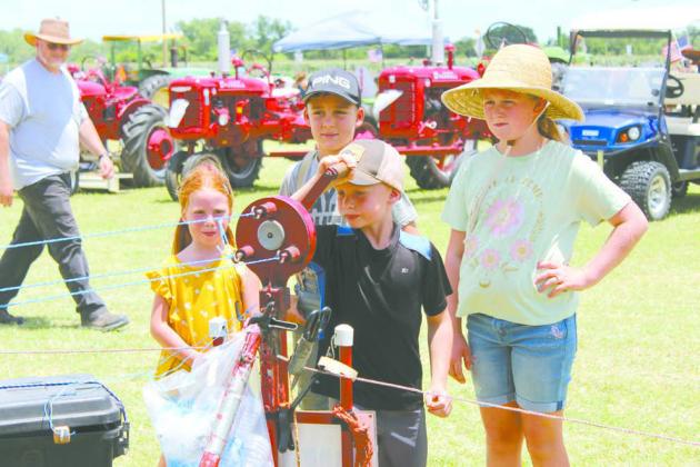 Judah Ramsey, 7, of Macomb, turns the rope-making machine owned by Danny Dunagan of McLoud, as his siblings watch at the 25th Annual Farming Heritage Festival, held at Shawnee Feed Center on June 22. The event is organized by the Shawnee Tractor and Engine Club. (See full cutline below.)