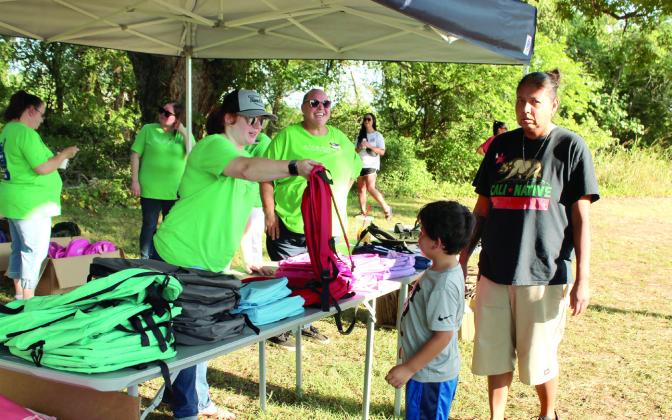 Tecumseh BancFirst Operations Specialist Ashlee Doss hands out backpacks full of school supplies during the Fifth Annual Tecumseh BancFirst Back to School Bash on July 30. Free hotdogs from BancFirst and snow cones from The Snow Shak were also available. The next BancFirst Back to School Bash will be at the Shawnee branch on Harrison today (Aug. 6), 6:15-7:30 pm. Photos by Natasha Dunagan, Countywide &amp; Sun