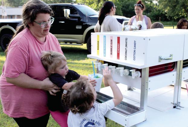 Mother, Rachael Caraway, and sister, Audrey Caraway, 4, both of Newalla, help Evelyn Caraway, 2, to add flavoring to her free snow cone from the Sno Shak during the Fifth Annual BancFirst Back to School Bash in McLoud on July 23. In addition to snow cones, BancFirst offered backpacks, filled with school supplies, and free hotdogs. McLoud FFA members volunteered at the event, as they have every year. The Back to School Bash will be held at Tecumseh's BancFirst, July 30, 6:15 - 7:30 pm, and Shawnee on Aug. 6.