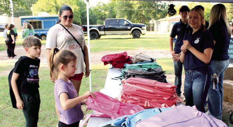 Incoming first-grader, Amber Williams, of McLoud, selects a pink backpack, as her brother, incoming fourth-grader, Zander Williams, and mother Jeannene Williams, as well as McLoud FFA volunteers, watch during the Fifth Annual BancFirst Back to School Bash in McLoud.