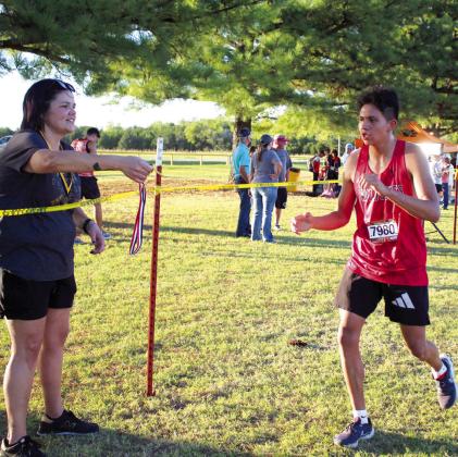 Retired Tecumseh counselor and coach Melissa Poole holds out a medal for Earlsboro sophomore Wes Lowe during the High School Boys 5K Run division of the Tecumseh Savage Cross Country Invitational