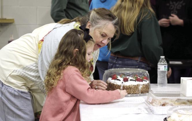 Jadie Goodson, 4, writes in her silent bid for a cake with the help of her grandmother, Linda Goodson.