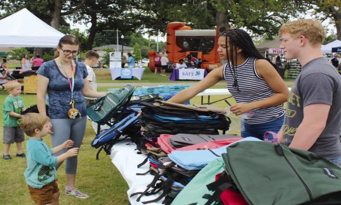 Khloe Tungate, the Youth Lead Volunteer Coordinator for the DGCG, hands a backpack to Jasper Batt, 3, of Shawnee, as fellow volunteer Colton Herron and Batt's mother, Andrea Batt, look on; Austin Batt, 5, in the background, also found a backpack.