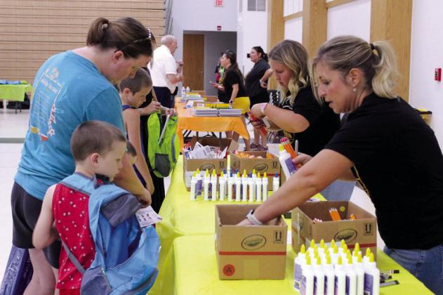 Elise Whitney, center, and her mother Hope Whitney add pencils and glue to backpacks during Mission Tecumseh's 11th Annual Back to School Bash.
