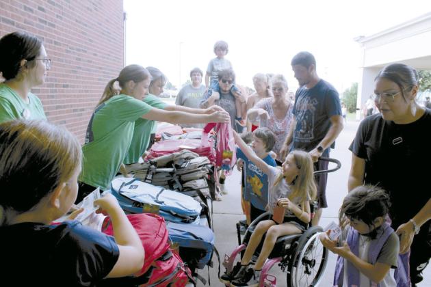 BancFirst employees Kim Pickard and Shannon Chandler hand backpacks to Nevaeh Mitchell, 9, of Shawnee, and her brothers Derric Jr., Wyatt, and Wade Mitchell, as her father, Derric Mitchell pushes her wheelchair during the Fifth Annual BancFirst Back to School Bash at the Harrison branch in Shawnee.