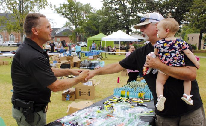Mark Withrow of Shawnee shakes hands with Pottawatomie County Sheriff Freeland Wood, as his granddaughter, Palmer Banks, one year, looks on during the Second Annual Hug-a-thon,.