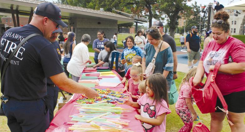 Shawnee Fire Department Sgt. Devin Abney hands Jerrica Reese, 4, of Shawnee, a ruler to add to her backpack, held by her mom Rachel Reese, during the Second Annual Hug-a-thon.