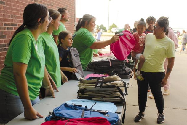 Shannon Chandler, BancFirst Regional Sales and Marketing Coordinator, hands a backpack to Ameerah Battise, 3, held by Tara Battise, both of Shawnee, during the Fifth Annual BancFirst Back to School Bash at the Harrison branch in Shawnee.