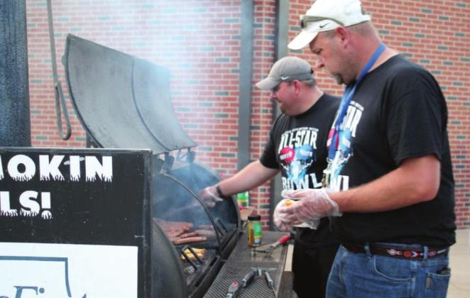 Tre Barlow, background, flips hotdogs, and Tracy Trussell adds cheese to the burgers during halftime of the CPN All-Star Bowl on June 3. Barlow and Trussell are both involved in Bethel Little League, which volunteered to work concessions this year. They are also in the Bethel Quarterback Club.