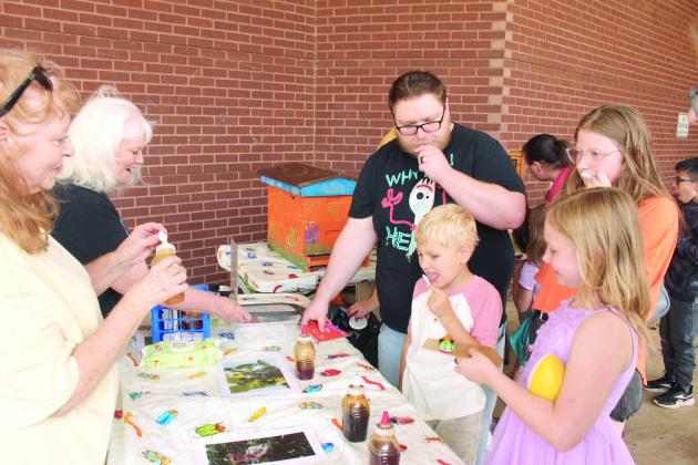 Matthew Sitton; Isaac Sitton; 6, Faith Sitton, 9; and, Elizabeth Sitton, 9, all of Shawnee, try different types of honey at the Central Oklahoma Honey Farm booth, assisted by Pamela Schantz and Gayla Doussett, during Bugfest at Shawnee Public Library on May 31. Rick Schantz, of Harrah, said the flavor of the honey depends on what type of nectar the bees eat. Natasha Dunagan, Countywide &amp; Sun