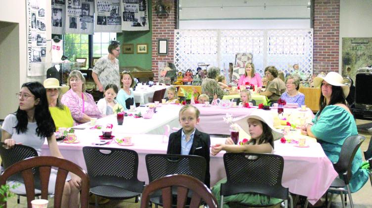 Attendees of the First Annual McLoud Historical Society Tea Party listen as Glenda Kuhn speaks about the polite way to fill a plate at a buffet and the Blackberry Princess and Junior Princess demonstrate. About 22 people, including several children, and five historical society members attended the new event at the McLoud Museum on May 3. Natasha Dunagan, Countywide &amp; Sun