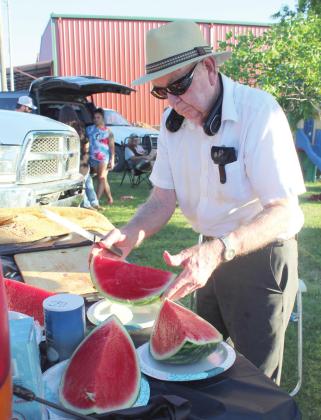 Lions Club member Jerry Bourassa slices a watermelon and places the slices on plates to give out during the Wanette Independence Day event on July 4. Bourassa brought 16 watermelons, as he has for several years.