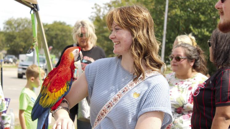 Tecumseh graduate Chloe Dawson holds a Scarlet Macaw on her arm at the Kids Zone booth of Ron and Susan Ham, of Shawnee, during Frontier Days. The Hams brought five of their 30 tropical birds, as well as a few Sulcata tortoises and a Bearded Dragon. Countywide &amp; Sun/Natasha Dunagan