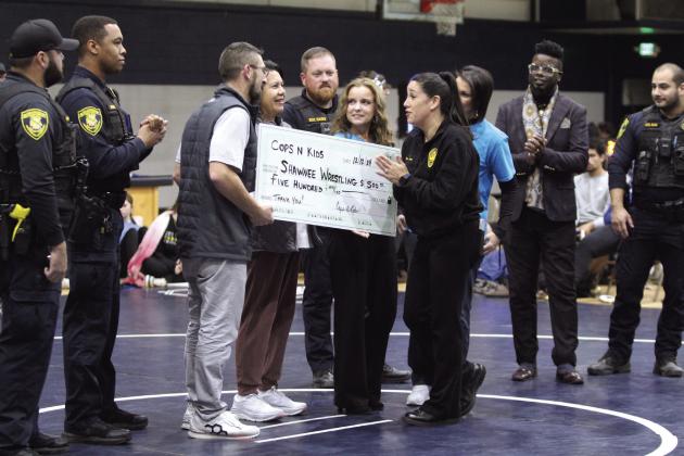 Vivian Lozano, the founder of Cops n' Kids, presents a check from the Cops n' Kids Board for $500 to Shawnee Wrestling Coach Andrew McCune for the Shawnee Wrestling Program during the home dual on Dec. 12. Lozano said the board plans to donate to different causes in the community every year. Present for the presentation, not in order, were board members Tara Andrews, Sally Coleman, Lisa Watson and Jeff Chamblain, as well as Jamelle Payne, Sgt. Rains, Cpl. Ruiz, Cpl. Price and PTL Arispe.