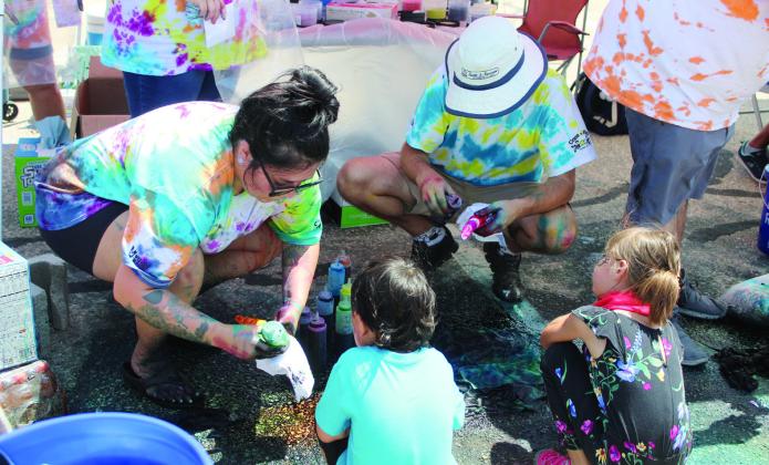 Sara Rose and Alan Geiger turn T-shirts into tie-dyed paintings for two children at the Vision Bank booth during the Sixth Annual Cops n’ Kids. The event attracted approximately 3,000 people. Countywide &amp; Sun/ Natasha Dunagan